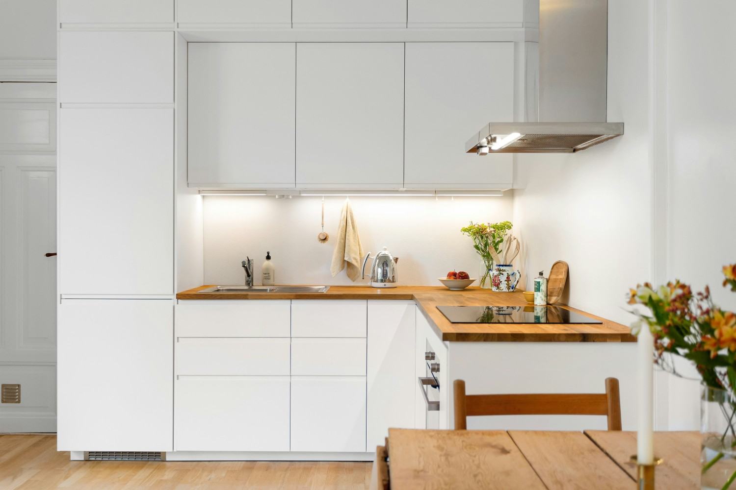 Cocina con muebles blancos, encimera de madera y barra de madera con una silla.