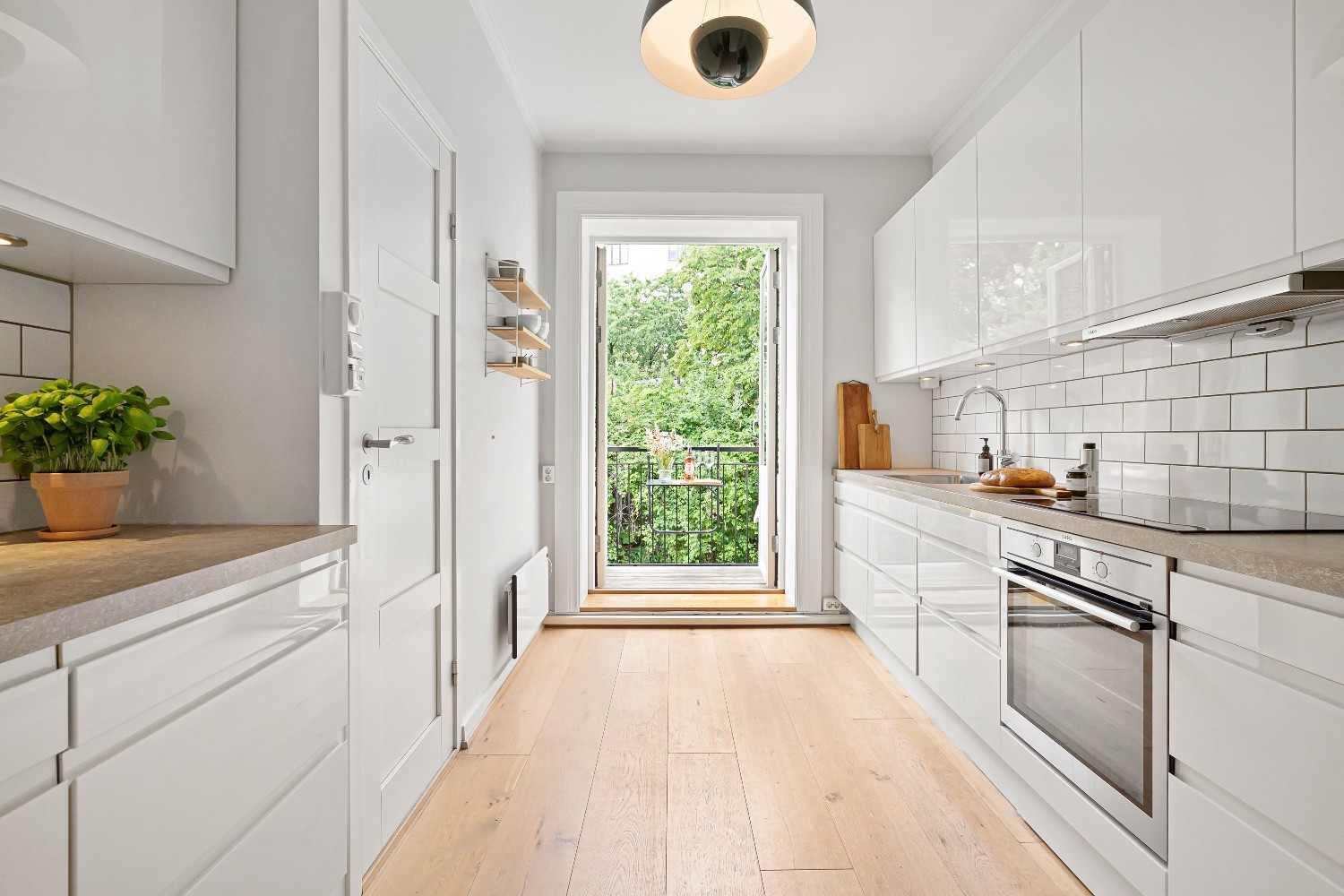 Cocina estrecha con muebles blancos en dos frentes, encimeras de madera y puerta acristalada al fondo.