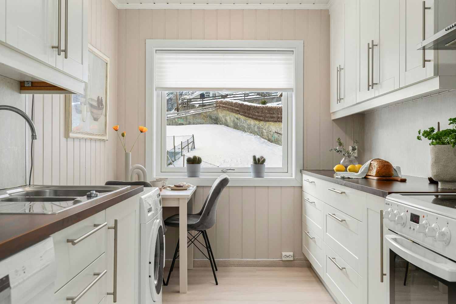 Cocina pequeña con muebles blancos y ventana sobre el fregadero.