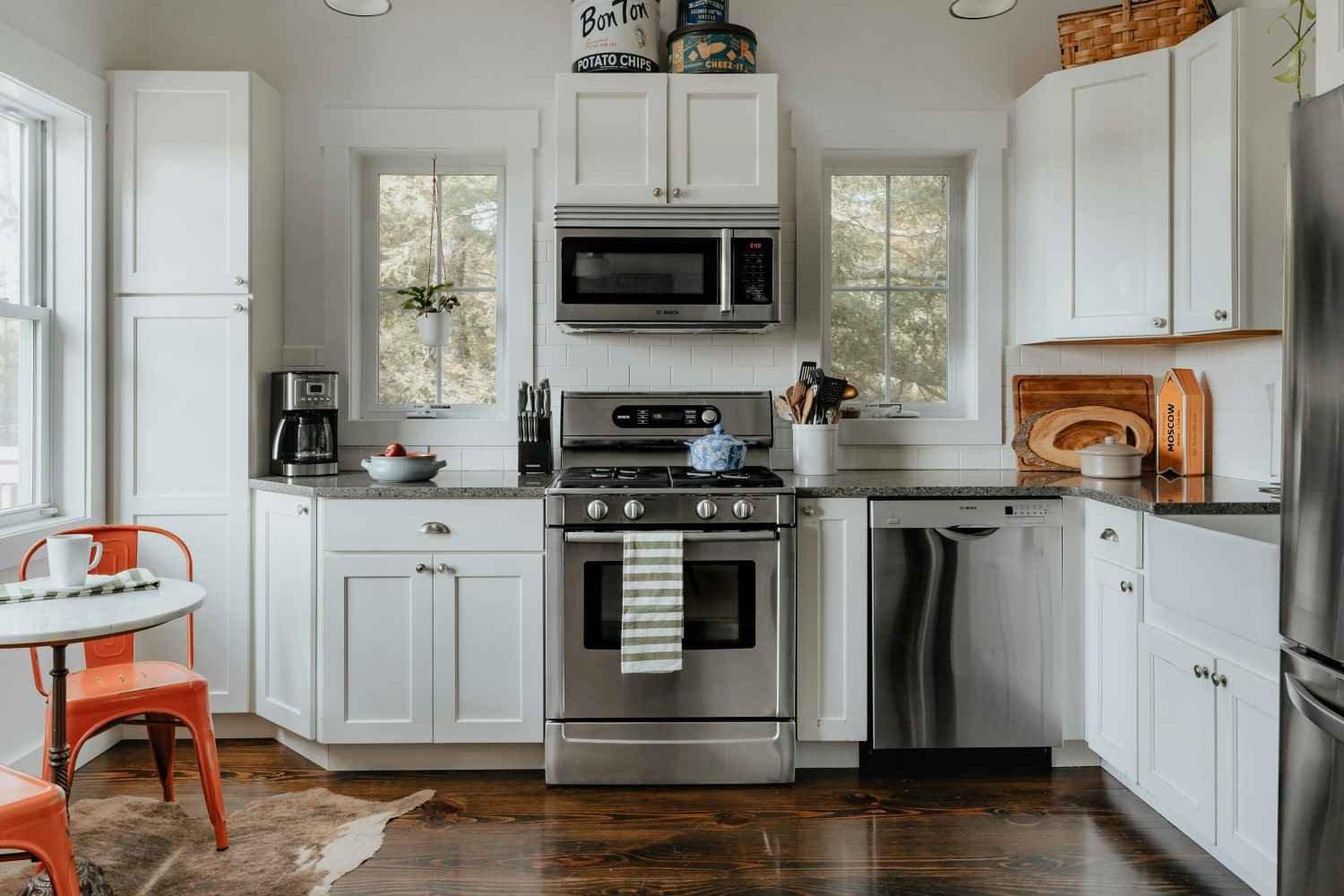CÓMO DECORAR UNA COCINA PASO A PASO Cocina con muebles blancos, encimera de madera, horno y microondas integrados y ventana sobre el fregadero.