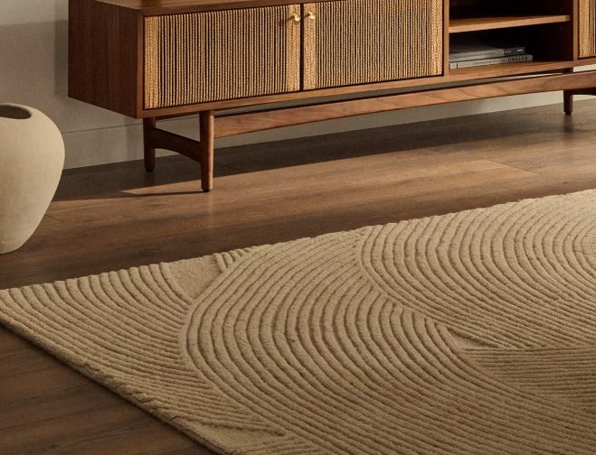 Detalle de una alfombra beige con líneas curvas en relieve junto a un sofá claro