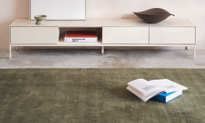 Alfombra verde oliva de diseño liso frente a un mueble bajo de color claro