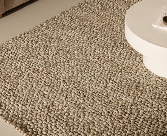 Detalle de una alfombra de tono gris cálido con textura de pequeños bucles junto a una mesa de centro blanca
