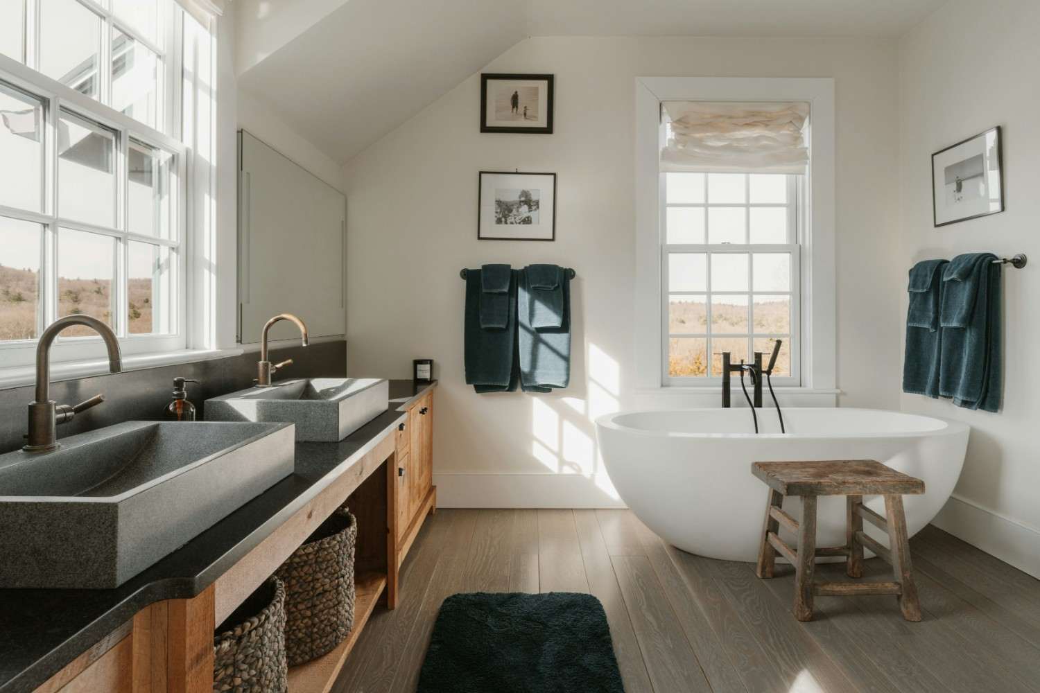 baño decorado con cestas y toallasBaño amplio con bañera exenta, mueble de madera con cestas, toallas y alfombra verde oscuro y taburete de madera.