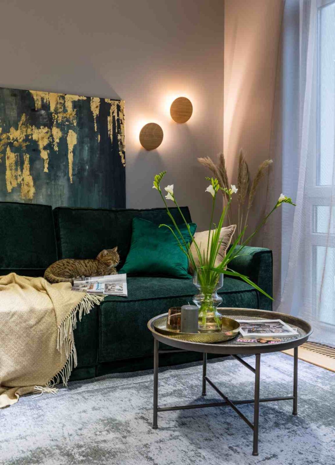 Cómo elegir un colchón Salón con sofá verde oscuro y dos apliques circulares encendidos que proyectan luz cálida sobre la pared.