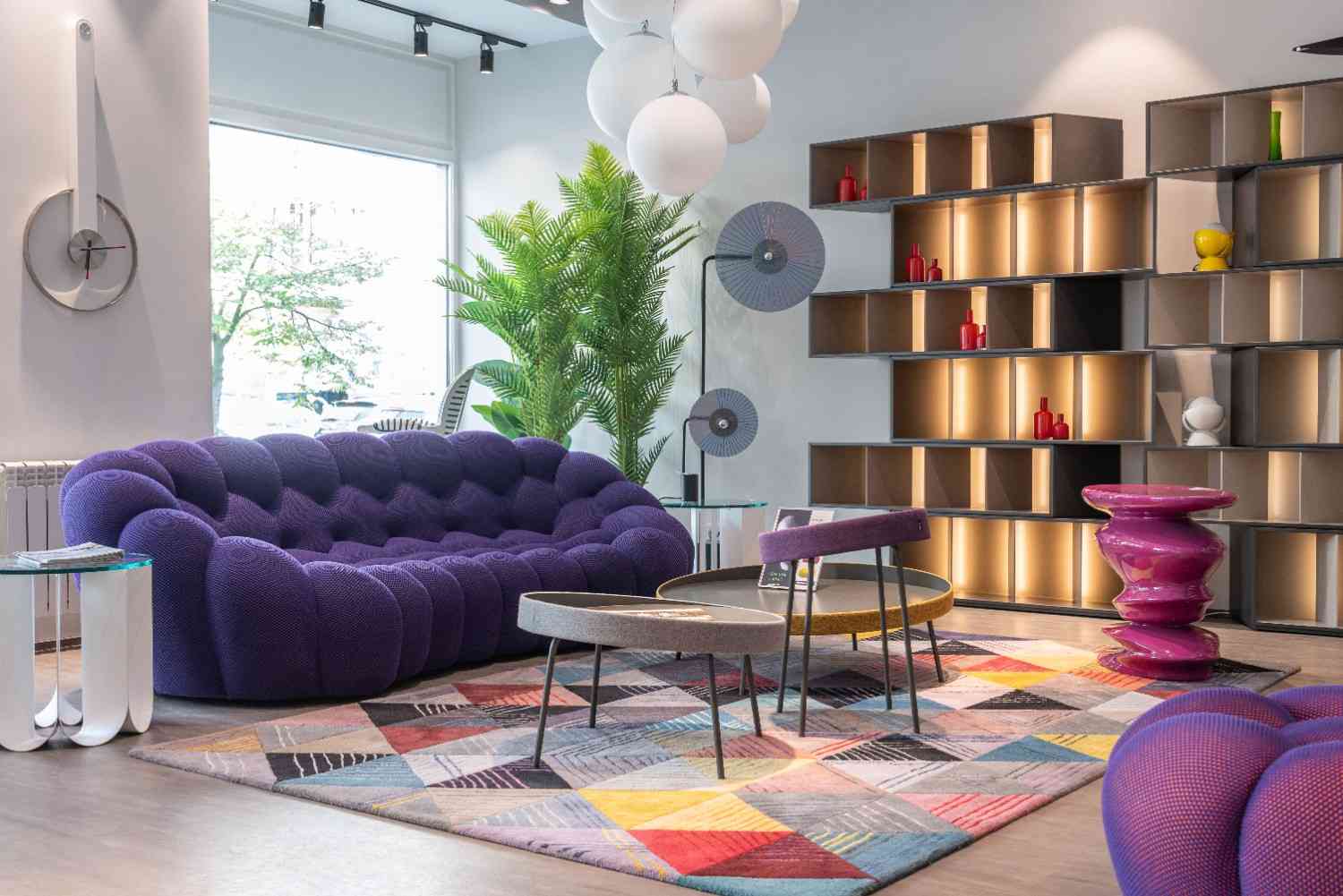 Alfombra rectangular con figuras geométricas multicolores bajo unas mesas de centro, junto a un sofá morado.