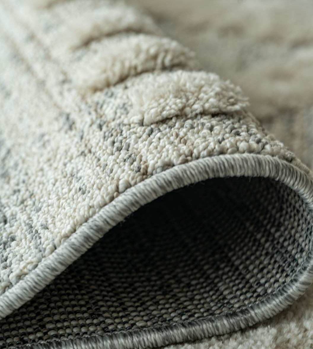 pexels atulm0han 18266459 100kbAlfombra beige doblada que muestra su textura en relieve, el borde rematado y el reverso.