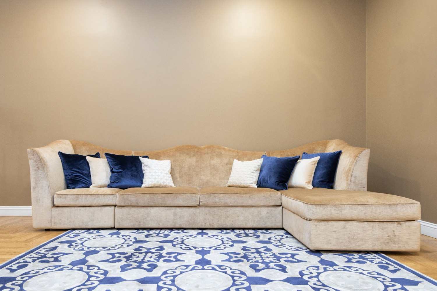 Sofá beige con chaise longue a la derecha de la imagen y cojines azules y blancos.