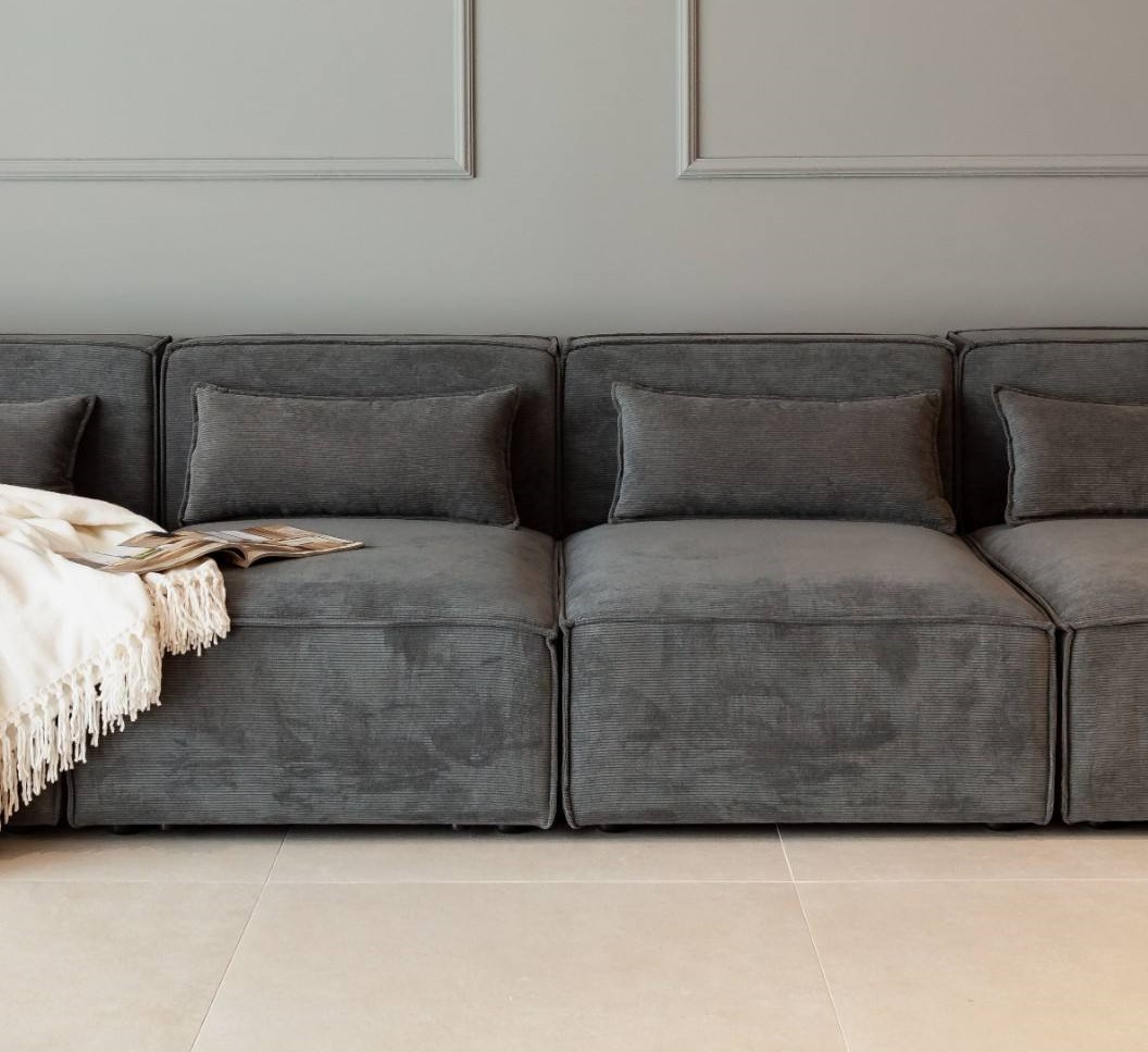Detalle de sofá modular gris con piezas individuales alineadas y cojines de respaldo.
